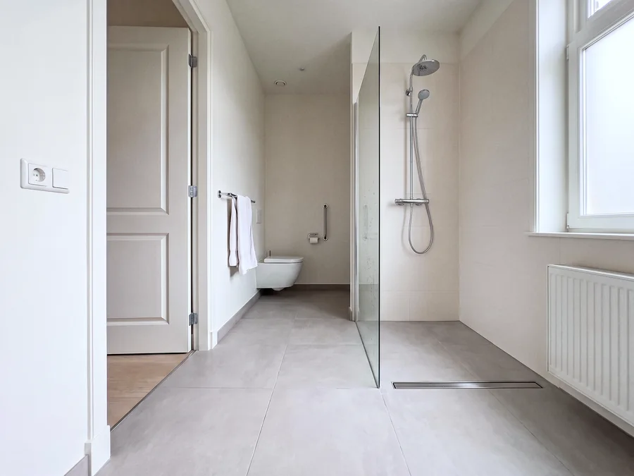 Een badkamer met een inloopdouche zonder drempel en een wc met steunbeugel.