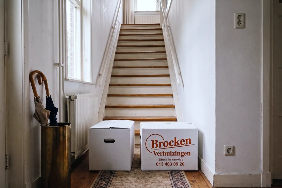 Een steile trap in een oudere woning met twee verhuisdozen onderaan.