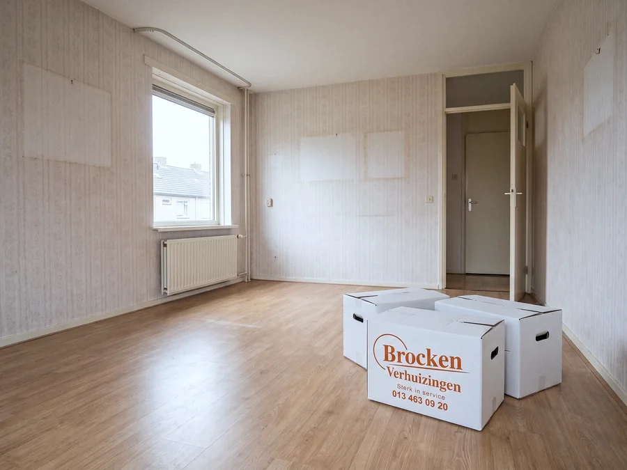 Een leeggehaalde woonkamer met lichte plekken op het behang en drie verhuisdozen bij de deur.