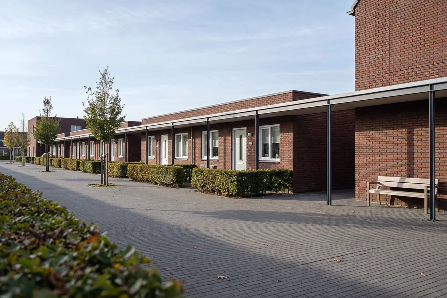 Een rij gelijkvloerse woningen met een overdekte loopgang naar een hoger bakstenen gebouw.
