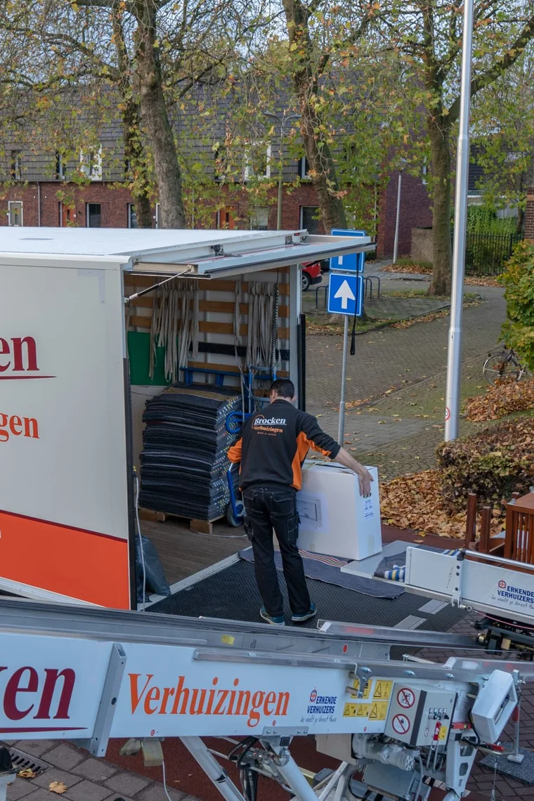 Verhuizer zet een doos in de open verhuiswagen van Brocken, met verhuisdekens in de laadruimte