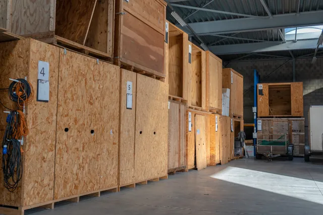 Genummerde houten opslagkisten en een oranje heftruck in de opslaghal van Brocken Verhuizingen