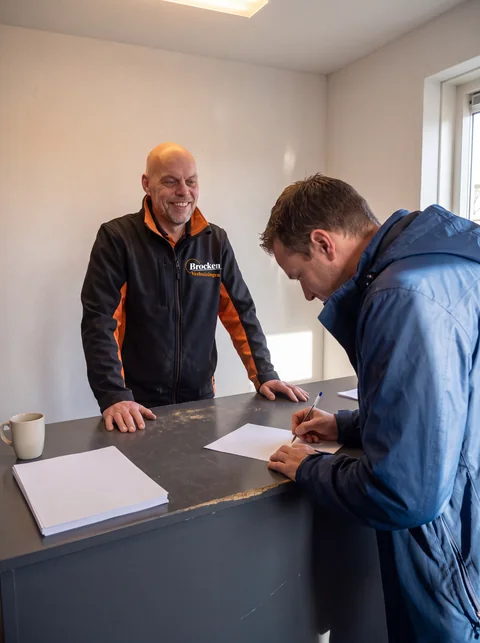 Klant tekent aan de balie van Brocken Verhuizingen de opdracht, terwijl een medewerker meekijkt