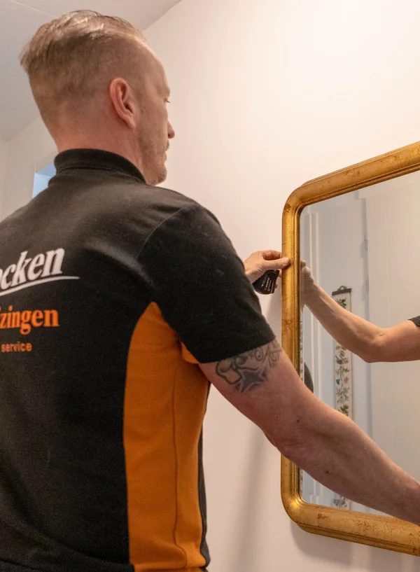 Verhuizer van Brocken Verhuizingen houdt een spiegel met gouden lijst tegen de muur