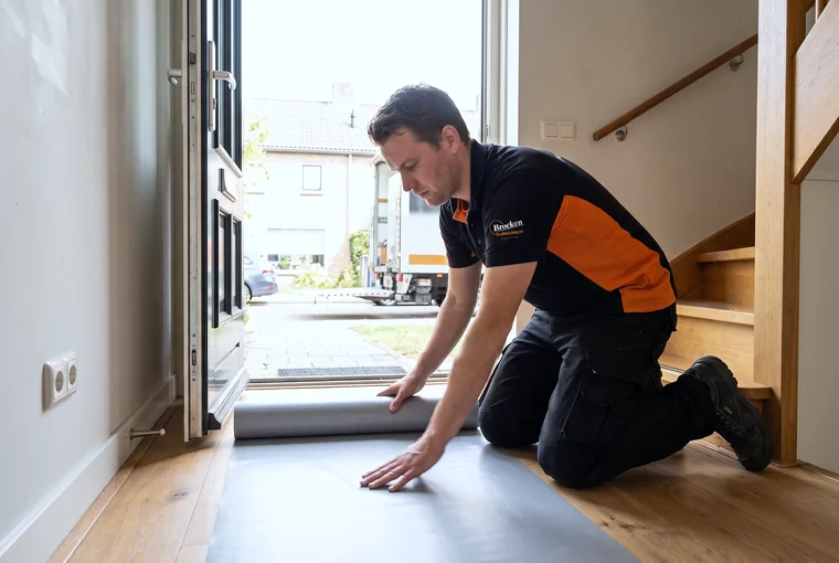 Verhuizer van Brocken Verhuizingen legt bij de voordeur vloerbescherming uit over de houten vloer van de hal