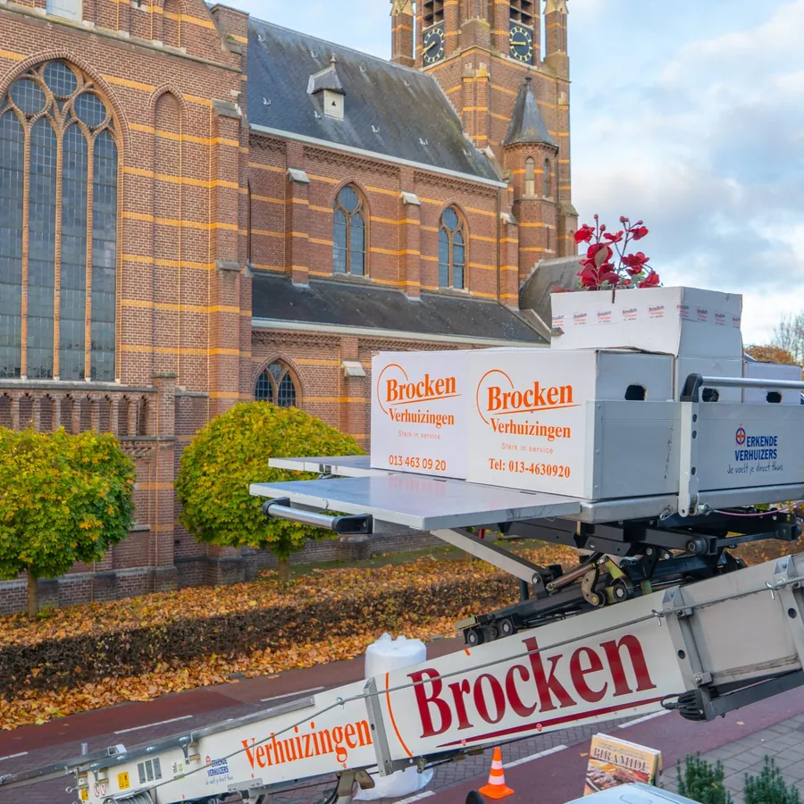 Liftplateau met verhuisdozen van Brocken Verhuizingen boven een kerkplein, met de liftarm met het logo op de voorgrond