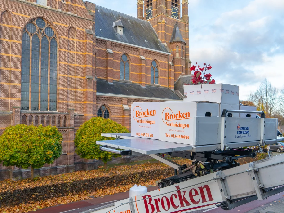 Verhuisdozen van Brocken Verhuizingen op het plateau van de verhuislift voor een kerk, met de sticker van Erkende Verhuizers