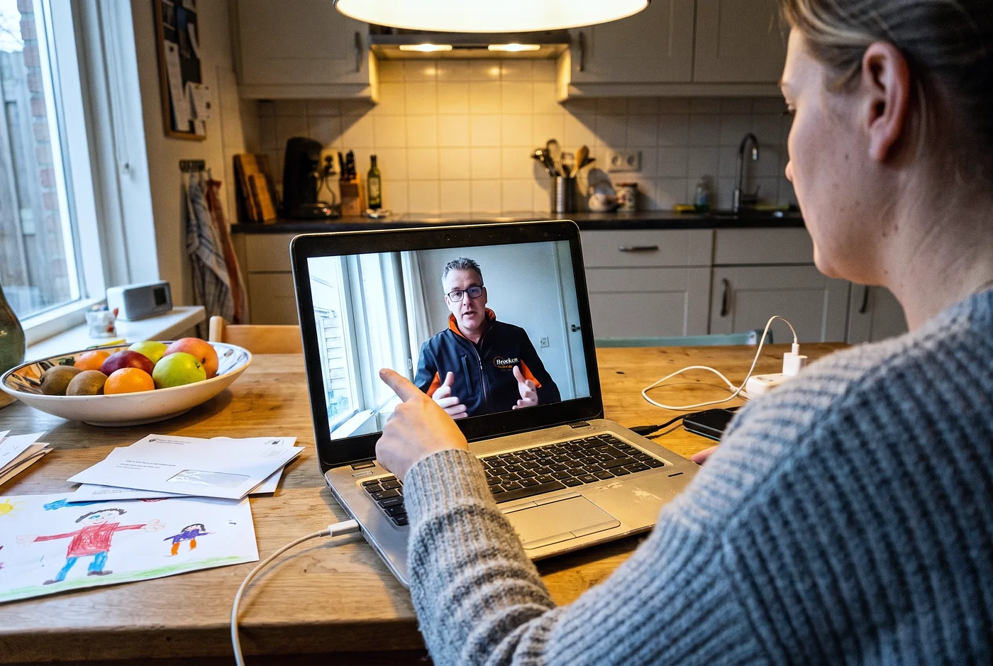 Een bewoonster aan de keukentafel in een videogesprek met een adviseur van Brocken Verhuizingen op haar laptop