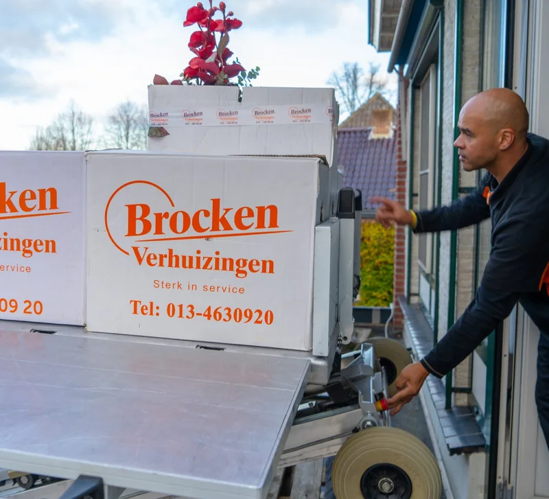 Verhuizer neemt verhuisdozen van Brocken Verhuizingen aan van het liftplateau bij een raam