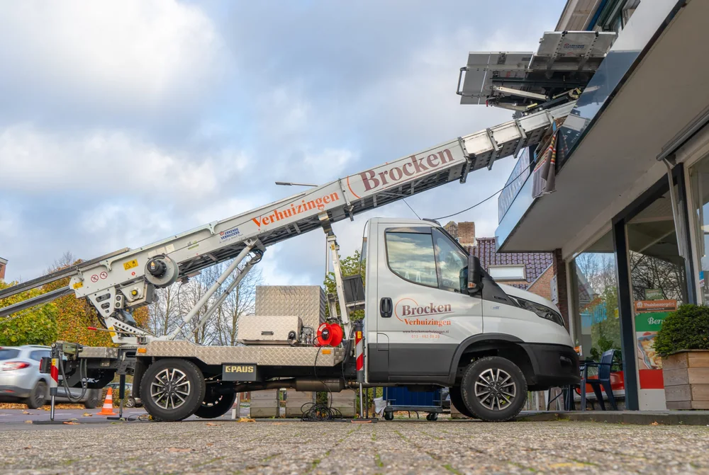 Bus van Brocken Verhuizingen met de ladderlift uitgeschoven naar een verdieping van een winkelpand
