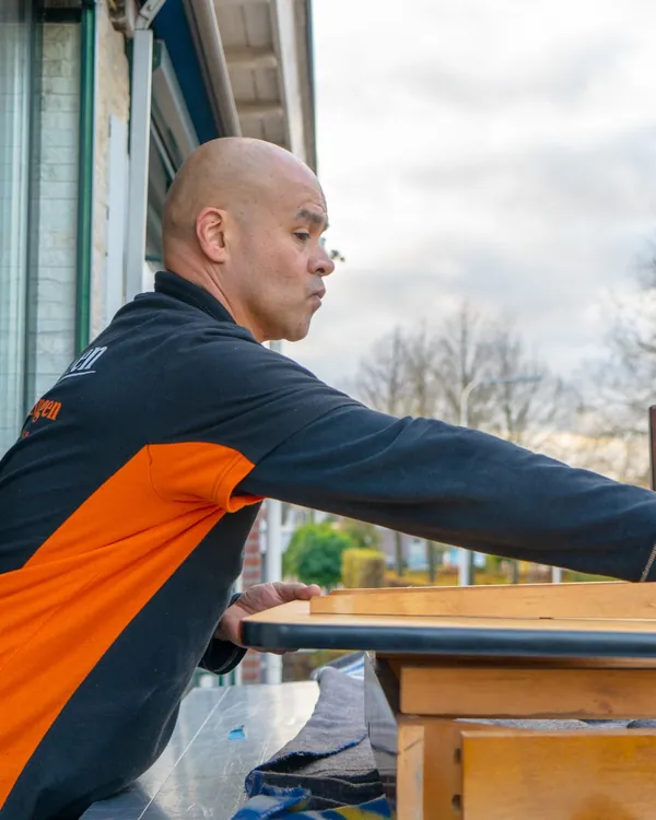 Verhuizer van Brocken Verhuizingen reikt over gedemonteerde meubels op het liftplateau bij een balkondeur