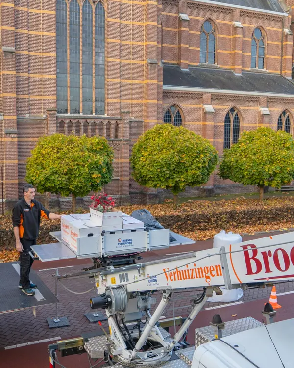 De liftarm met het logo van Brocken Verhuizingen en een verhuizer bij de wagen op het plein, van bovenaf gezien