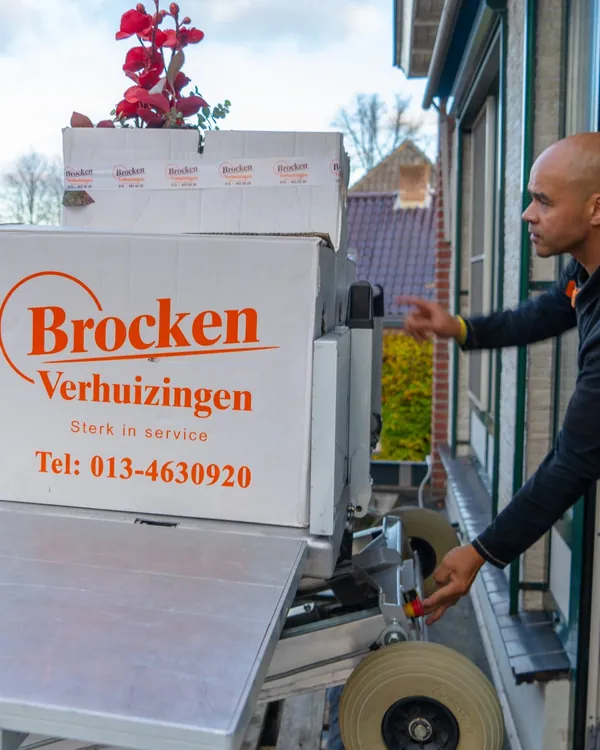 Verhuizer van Brocken Verhuizingen neemt verhuisdozen aan van het liftplateau bij een raam op een verdieping