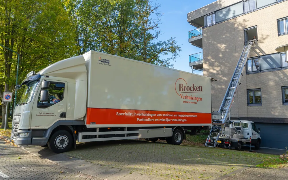 Vrachtwagen van Brocken Verhuizingen met de uitgeschoven verhuislift tegen een appartementengebouw