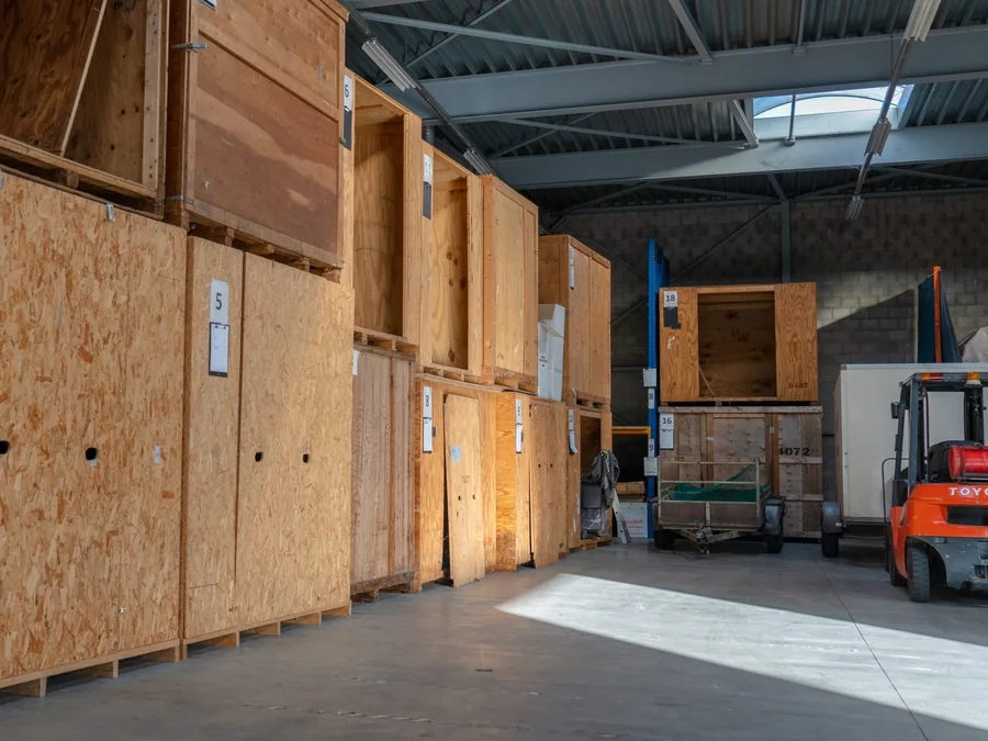 Rijen houten opslagkisten met nummers in de opslaghal van Brocken Verhuizingen, met een oranje heftruck