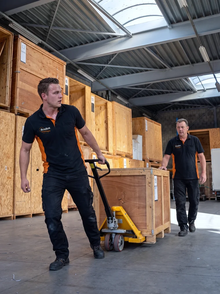 Verhuizer van Brocken Verhuizingen trekt met een palletwagen een houten opslagkist door de opslaghal