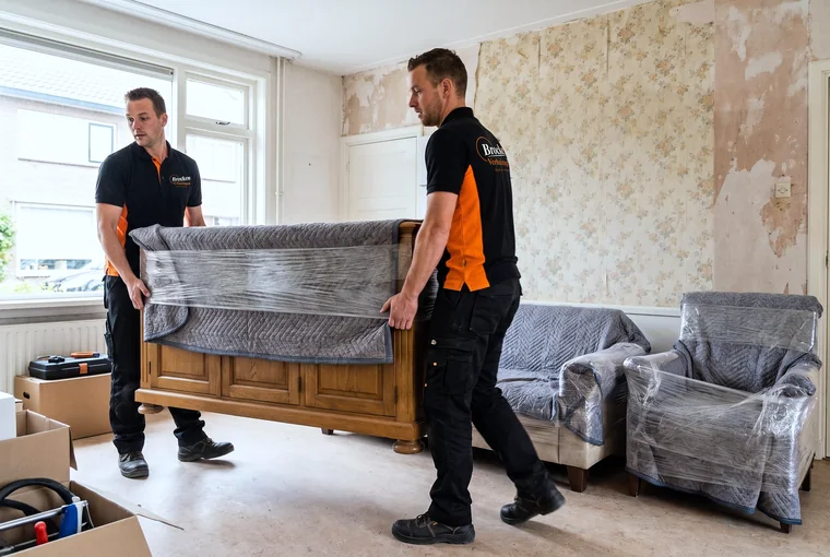 Twee verhuizers van Brocken Verhuizingen dragen een ingepakt dressoir uit een woonkamer die verbouwd gaat worden