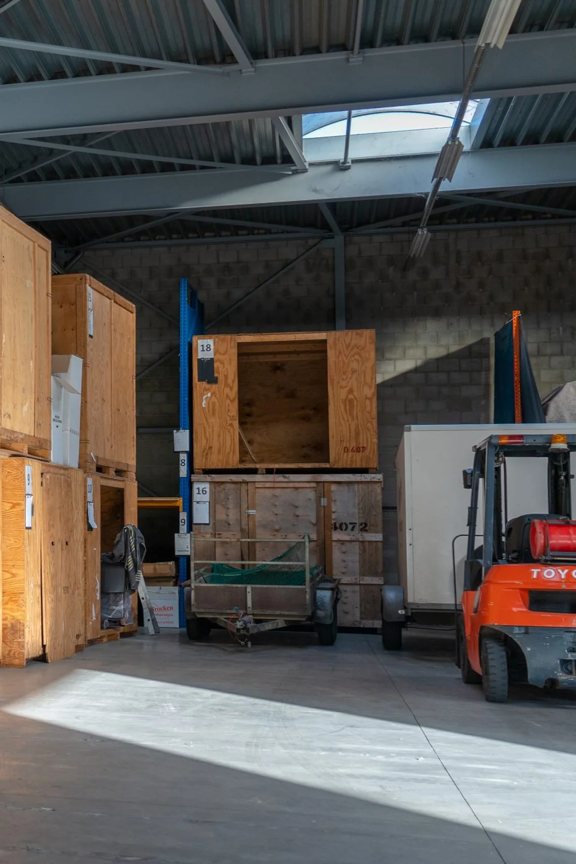 Opslaghal met genummerde houten opslagkisten, een stelling en een oranje heftruck