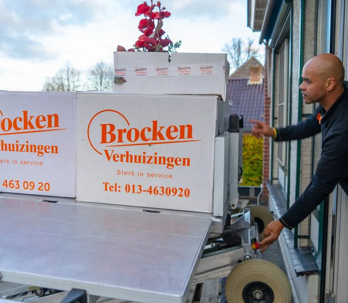 Een verhuizer van Brocken Verhuizingen neemt bij het open raam verhuisdozen aan van het plateau van de verhuislift