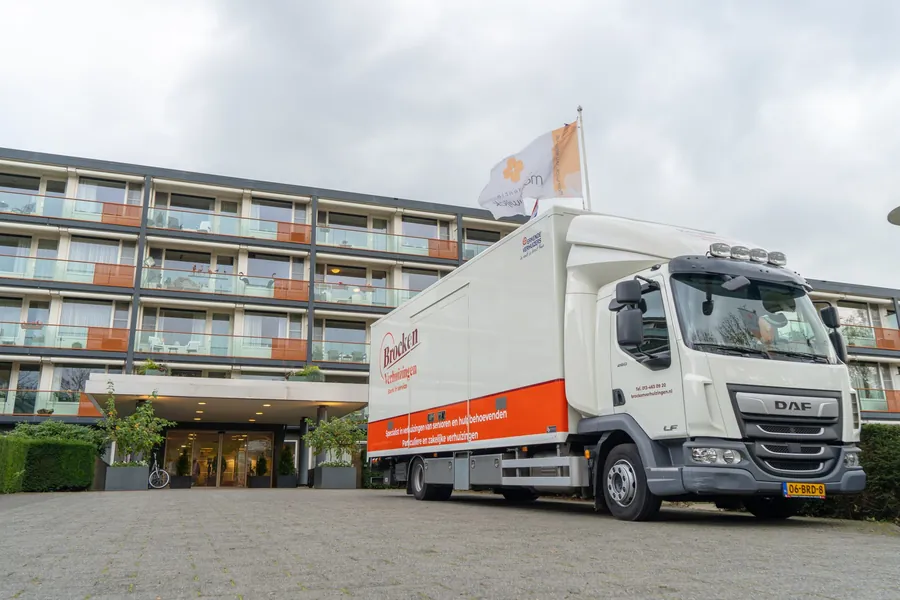 Verhuiswagen van Brocken Verhuizingen voor de ingang van een woonzorgcomplex met balkons
